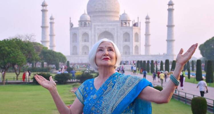 Vrouw in traditionele kleding poseert met opgeheven handen voor de Taj Mahal.