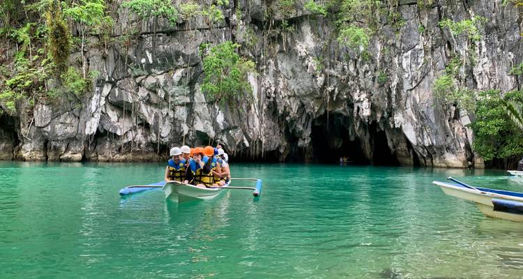 Personas en un bote dirigiéndose hacia una cueva con agua azul cristalina.