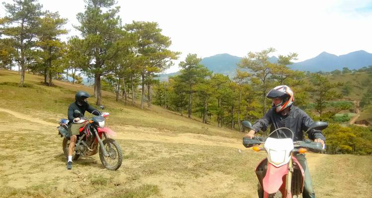 Deux personnes sur des motos sur une piste de terre entourée d'arbres.