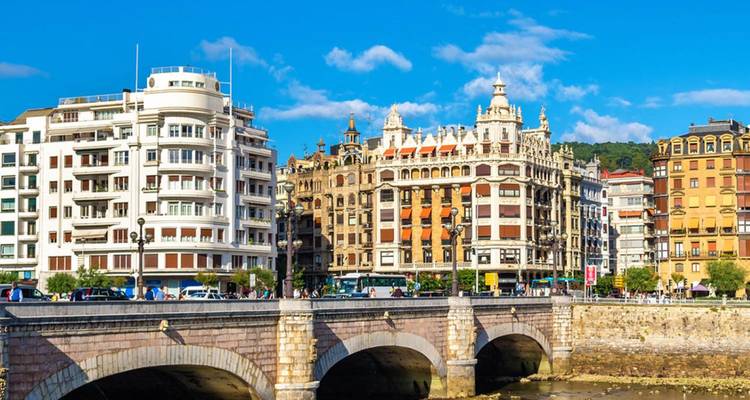Elegantes edificios históricos y puente de piedra sobre un río en Bilbao en un día soleado.