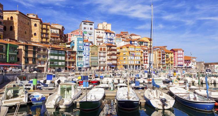 Puerto pesquero colorido lleno de barcos y edificios multicolores a lo largo del malecón bajo cielos azules.