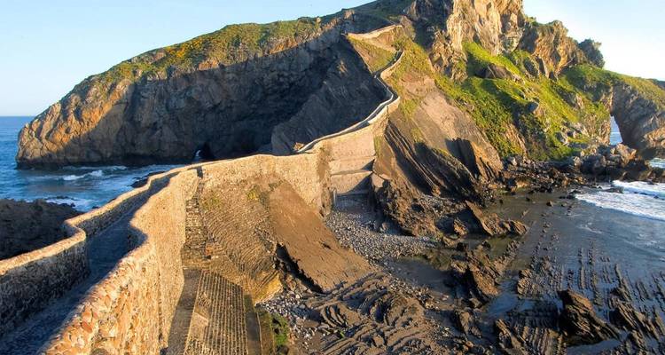 Sendero de piedra serpentea hacia la ermita en la isla de San Juan de Gaztelugatxe con olas abajo.