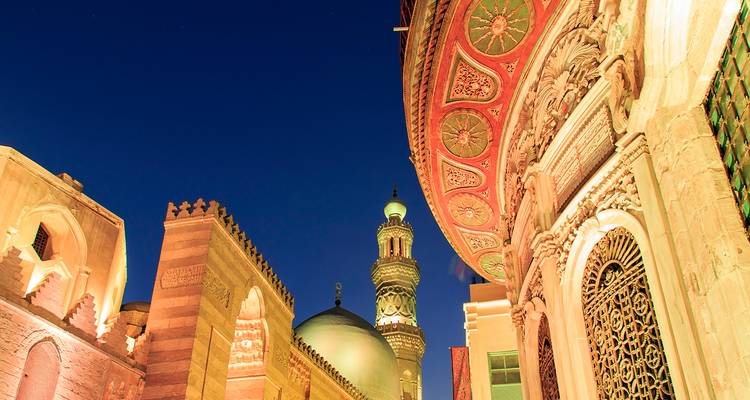 Nachtelijke aanzicht van sierlijke islamitische architectuur en minaret verlicht tegen een diepblauwe Caïro-hemel.