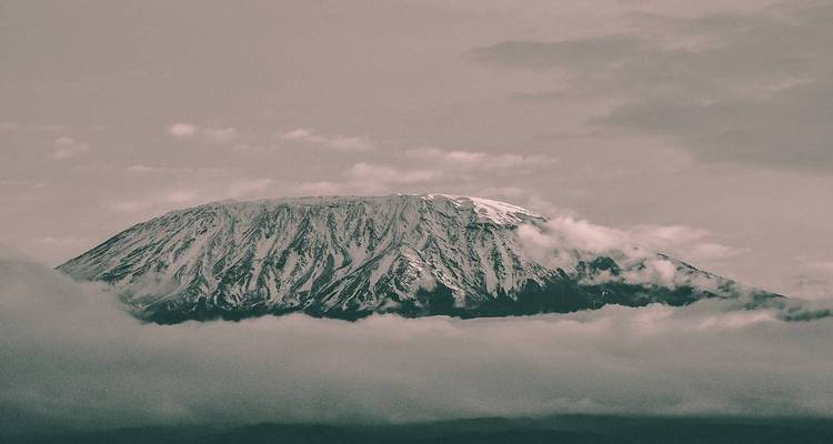 Le mont Kilimandjaro avec ses sommets enneigés entourés de nuages.