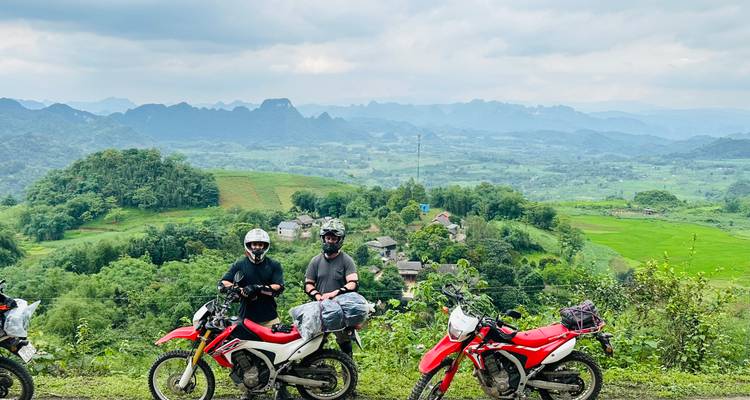 Two motorcyclists with a panoramic view of lush valleys.