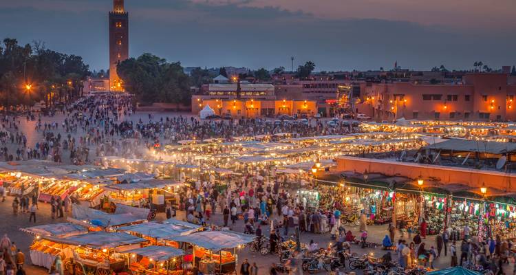 Scène de marché du soir avec des étals et des lumières dans une place animée.