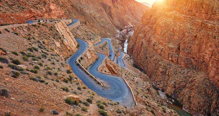 Route sinueuse traversant un canyon avec la lumière du soleil projetant des ombres.