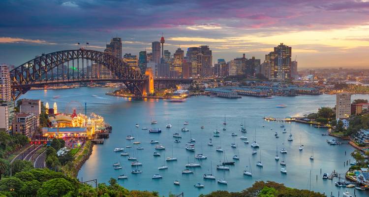 Die ikonische Sydney Harbour Bridge und die Skyline der Stadt überblicken bei Sonnenuntergang Boote.