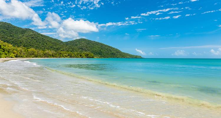 Playa prístina con agua cristalina y exuberantes colinas verdes.