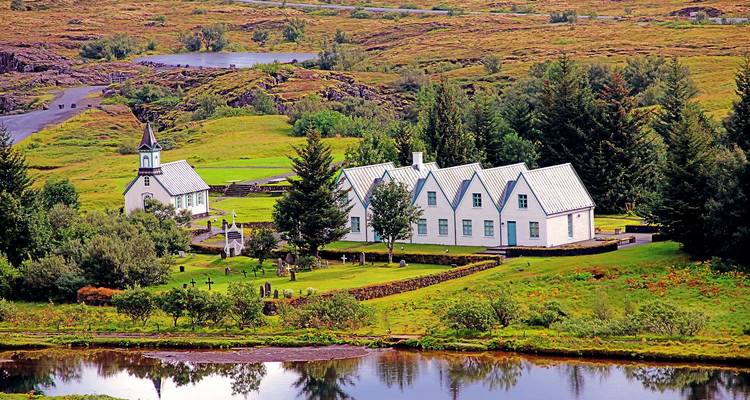 White church and farmhouse cluster amid green meadows and rivers in Thingvellir National Park.