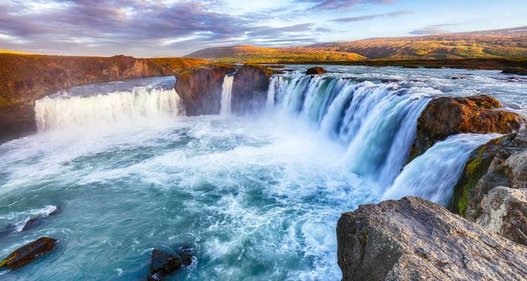 Powerful Goðafoss waterfall thundering into a turquoise river under golden evening light