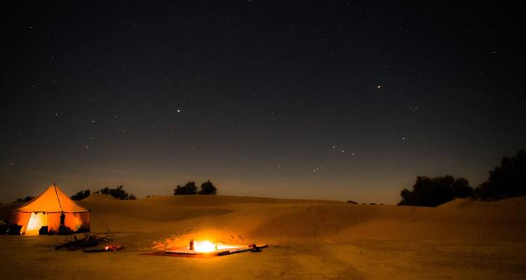 Feu de camp et tente sous un ciel étoilé dans le désert.