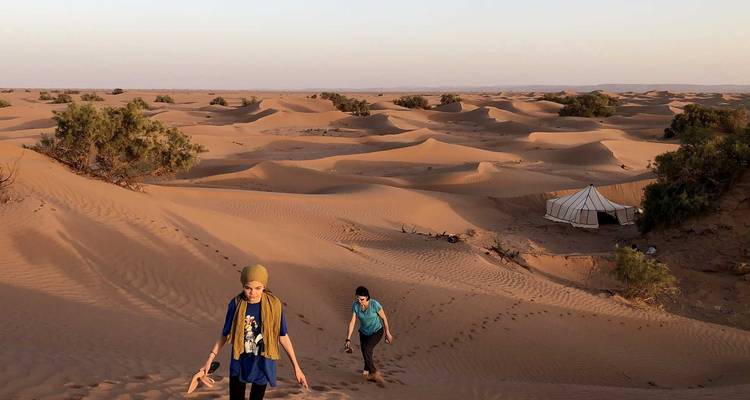 Deux personnes marchant dans le désert avec une tente au loin.