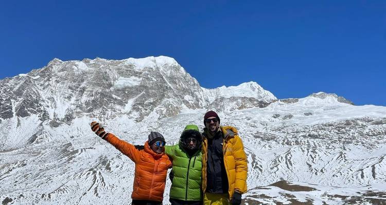 Drie mensen in kleurrijke jassen die voor besneeuwde bergen staan.