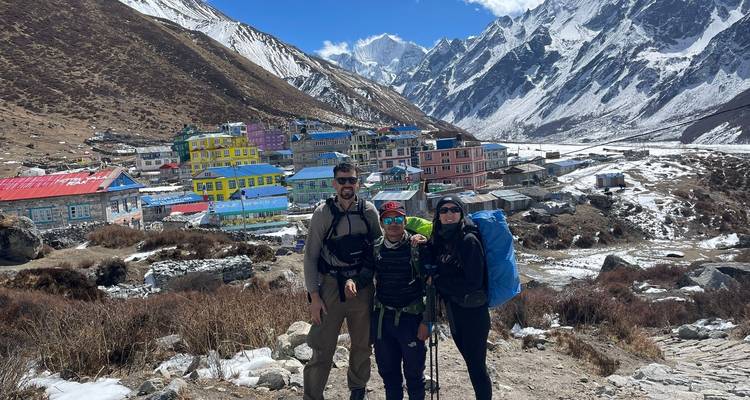Wandelaarstrio voor levendig dorp omringd door bergtoppen.