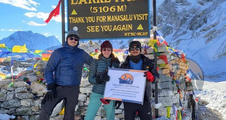 Three people at a high-altitude sign with snow and mountains.