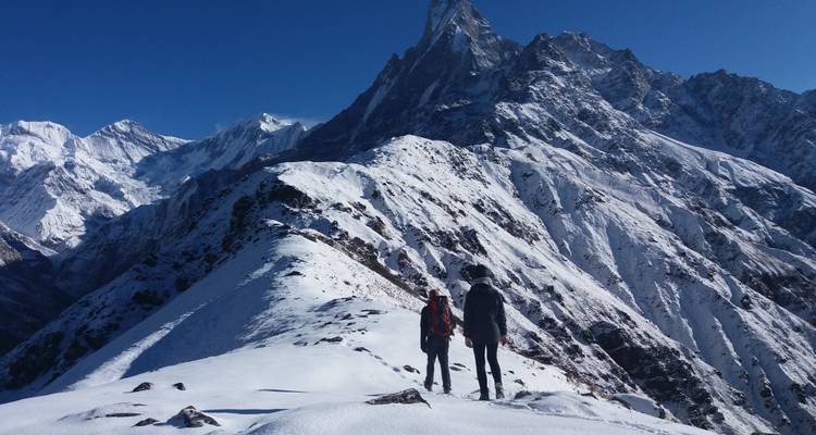 Twee trekkers die langs een besneeuwde bergkam in de Himalaya lopen.