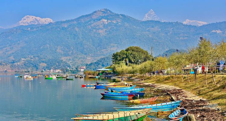 Des bateaux colorés sur le rivage d'un lac avec des montagnes en arrière-plan.