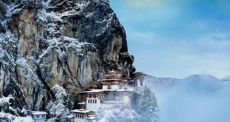 Vue d'un monastère couvert de neige sur une falaise au milieu de montagnes brumeuses.