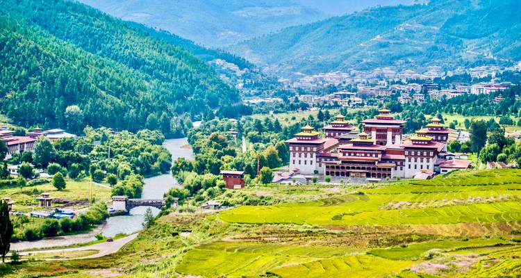 Vue panoramique d'une vallée avec une grande forteresse et une rivière avec des collines vertes.