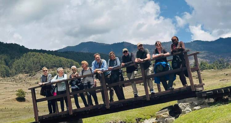 Groupe de personnes posant sur un pont en bois avec des montagnes pittoresques en arrière-plan.
