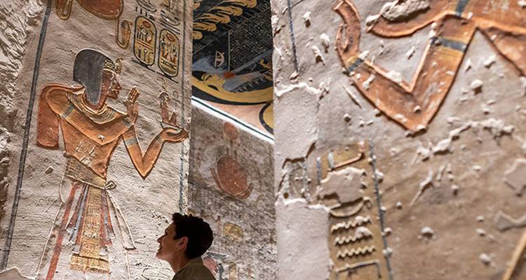 Visiteur contemplant les gravures murales hiéroglyphiques colorées à l'intérieur d'une tombe égyptienne antique.