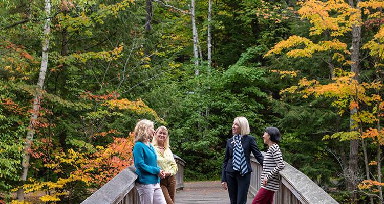 Groupe de femmes bavardant sur un pont en bois entouré d'une forêt d'automne colorée.