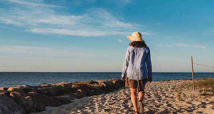 Woman wearing a sunhat strolls along a sandy beach path beside the Atlantic.