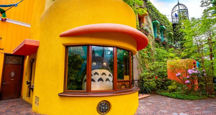 Leuchtend gelbe gekrümmte Fassade des Ghibli-Museums mit einer Totoro-Figur, die aus einem Fenster schaut.