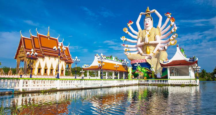 Templo colorido y gran estatua de deidad cerca de un cuerpo de agua.