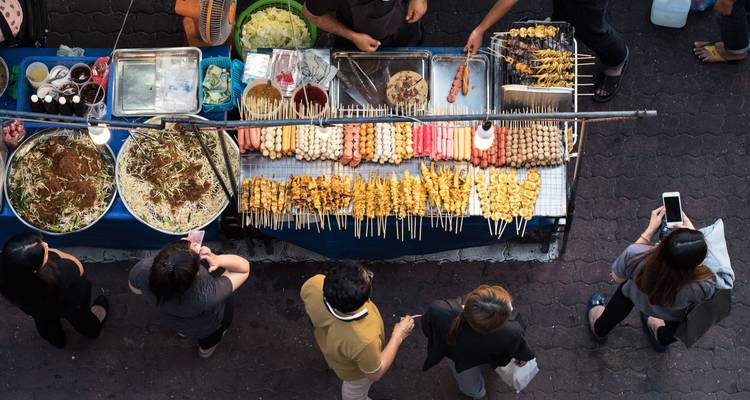 Mercado de comida callejera con varios pinchos y gente caminando.
