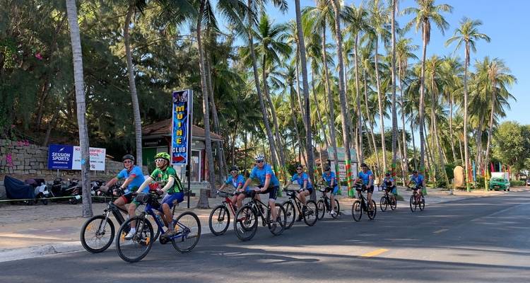 Groep fietsers die door een straat rijdt die omzoomd is met palmbomen.