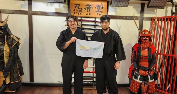 Zwei Personen in Ninja-Kostümen halten ein Banner in einem Raum.