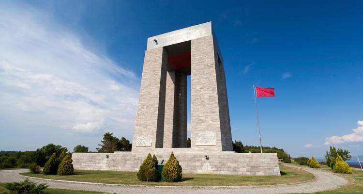 Monumento con una gran bandera roja en un entorno de parque.