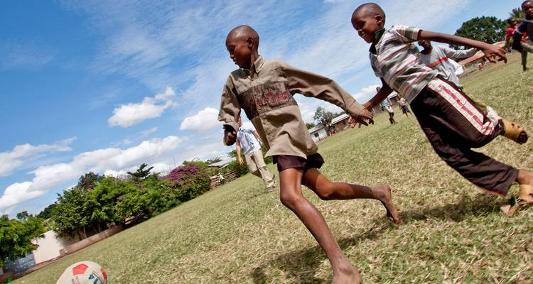 Des enfants du coin qui courent pieds nus en jouant au football sur un terrain herbeux sous un ciel bleu
