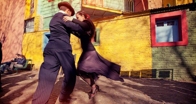 Una pareja de tango elegante bailando en las piedras contra paredes pintadas con colores vibrantes en La Boca.