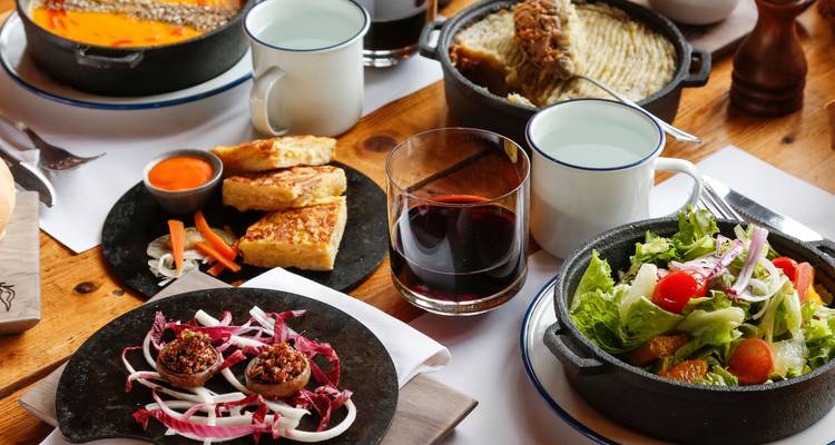 Rustieke houten tafel vol met hartige gerechten, salade, wijn en gedeelde borden