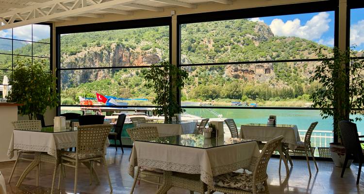 Riverside café interior with open glass walls looking onto green hills and water.