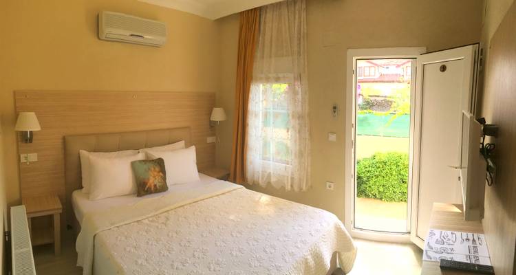 Simple hotel bedroom with neutral décor and sunlight filtering through sheer curtains.