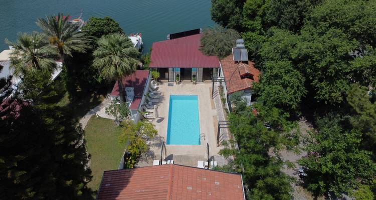 Aerial view of a small villa compound with central swimming pool beside a river.