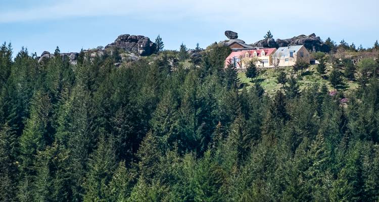 A forested mountain slope topped by granite boulders and a few isolated cottages.