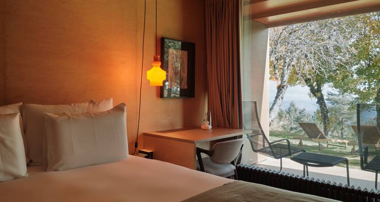 Cozy hotel room with soft lighting and a balcony view to a leafy garden and loungers.