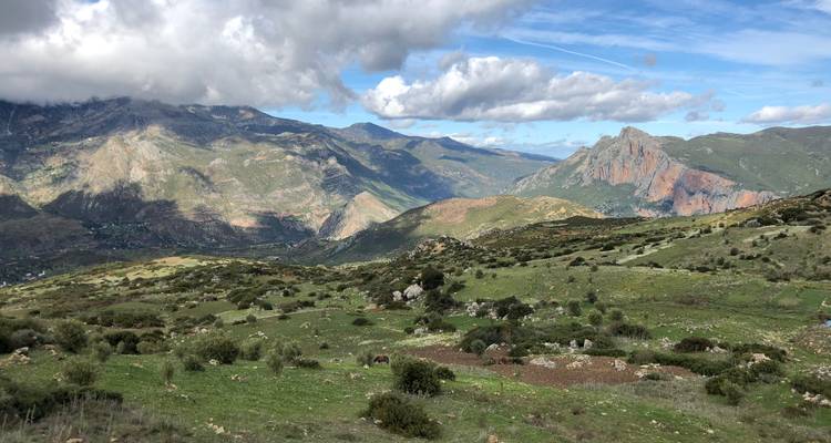 Heuvels en bergen met een lappendeken van velden en wolken erboven.