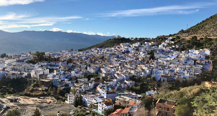 Stad op een heuvel met iconische blauwe gebouwen, schilderachtige bergen in de verte.