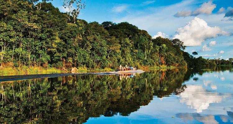 Boot auf einem Fluss durch einen üppigen Regenwald mit Spiegelungen im Wasser.