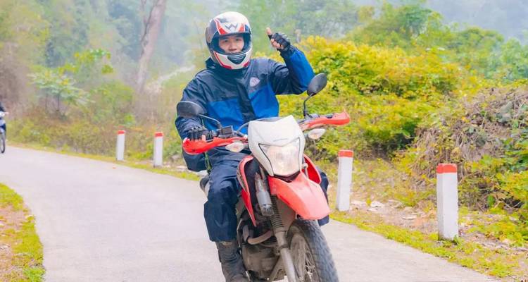 Een motorrijder die een duim omhoog geeft tijdens het rijden op een weg omgeven door groen.