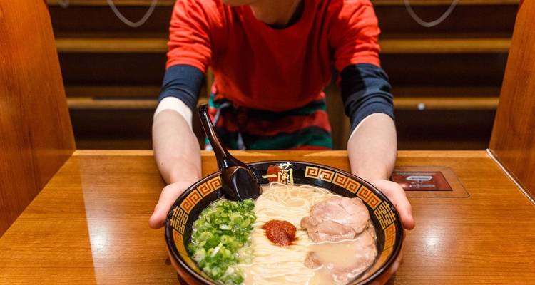 Kom ramen die wordt geserveerd door een kok in een rood shirt.
