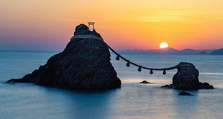 Zonsondergangzicht van twee heilige rotsen in de zee met een Shinto torii-poort.