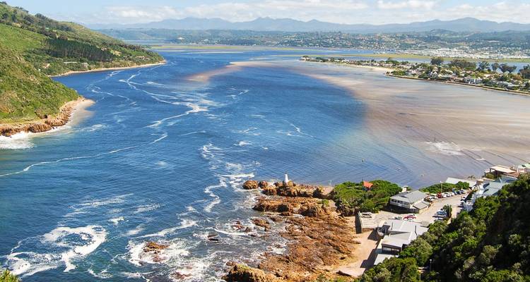Luftaufnahme der lebendigen blauen Lagune, die sich an den Knysna Heads mit dem Meer trifft, mit entfernten Küstenbergen im Hintergrund.