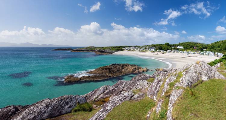 Zandstrand met turquoise wateren en rotsformaties.